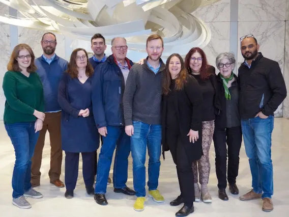 Members of the GHHIN Management Committee pose in front of a white tornadic sculpture and a gray and white marble wall.