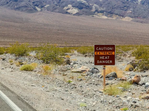 A sign on the side of a desert road reads, "Caution! Extreme Heat Danger"