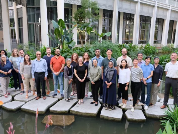 Heat experts pose for a group photo on stepping stones in a pond in front of the Yale-NUS building.