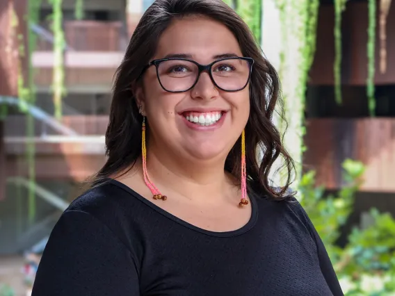 Carolina smiles in black framed glasses, a black shirt and beaded earrings at U of A's ENR2 building.