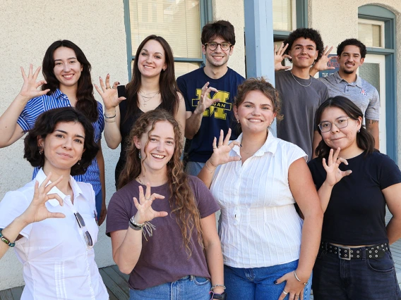 Nine of the 10 2025-26 Mo's Policy Scholars flash wildcat hand signs on the steps of the Udall Center