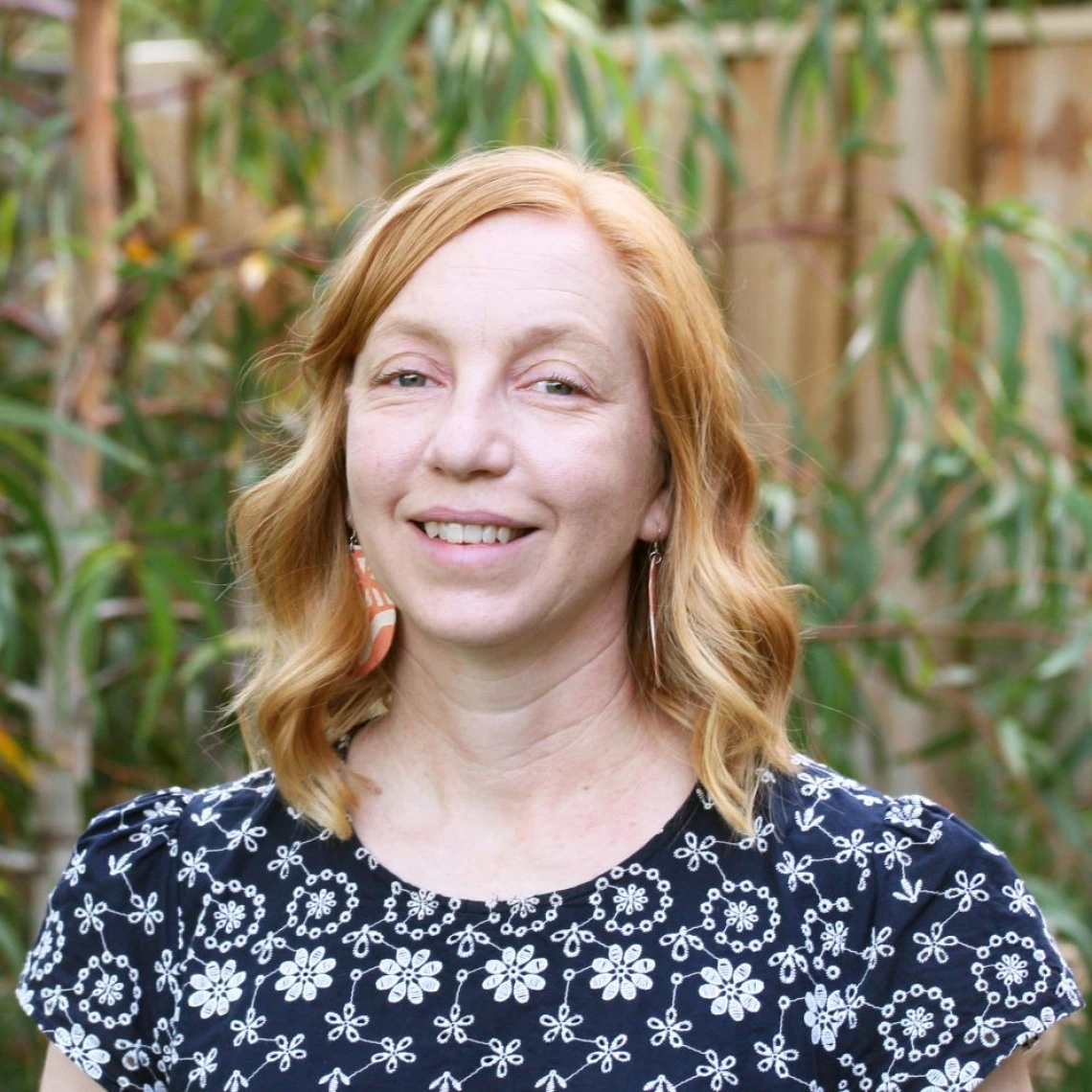 Portrait of Natasha Pauli outside with a Woden fence and green plants behind her.