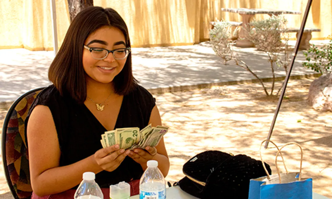 A young woman counts cash and smiles after participating in a 2019 NAYEP market event.