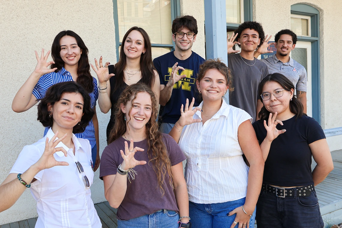 Nine of the 10 2025-26 Mo's Policy Scholars flash wildcat hand signs on the steps of the Udall Center