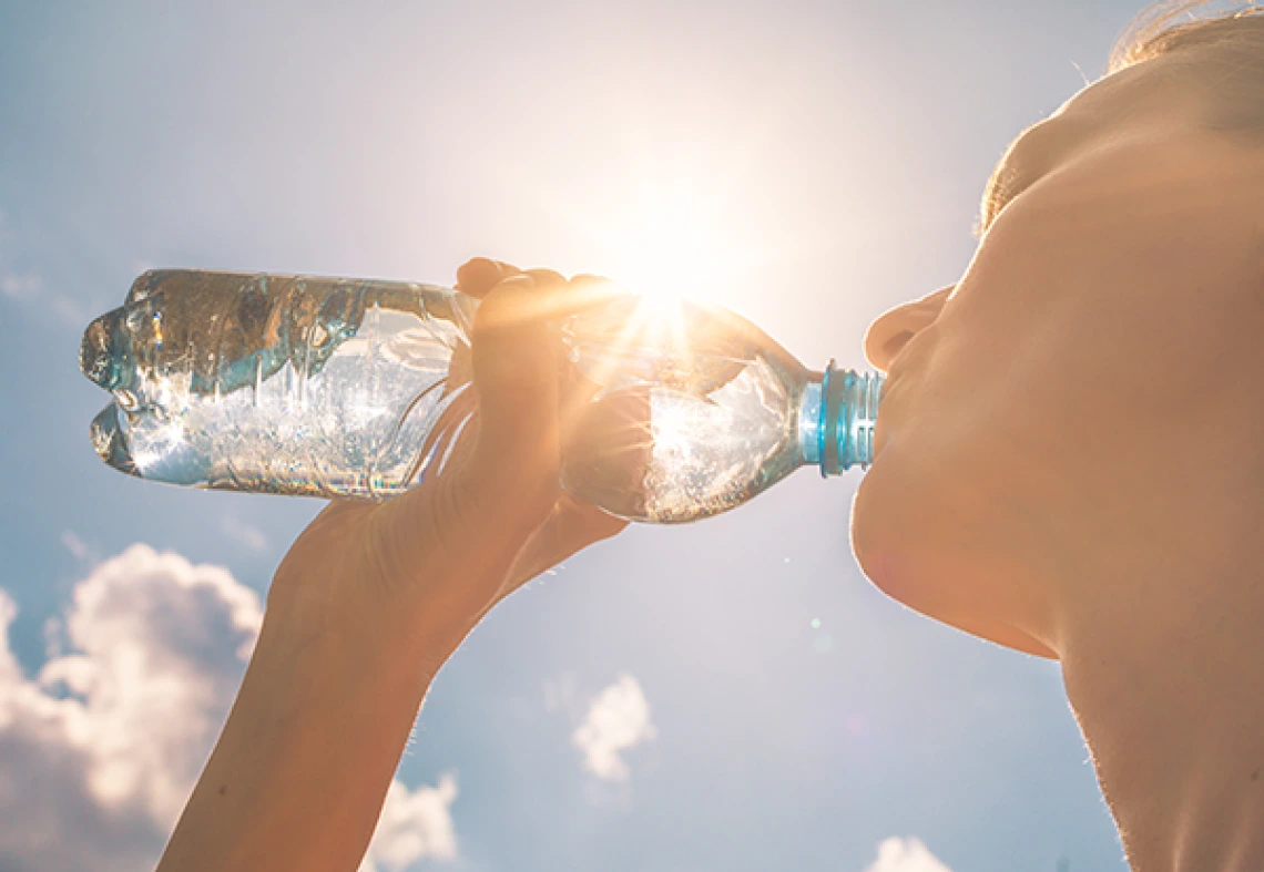 a woman drinks from a clear water bottle with the sun behind it