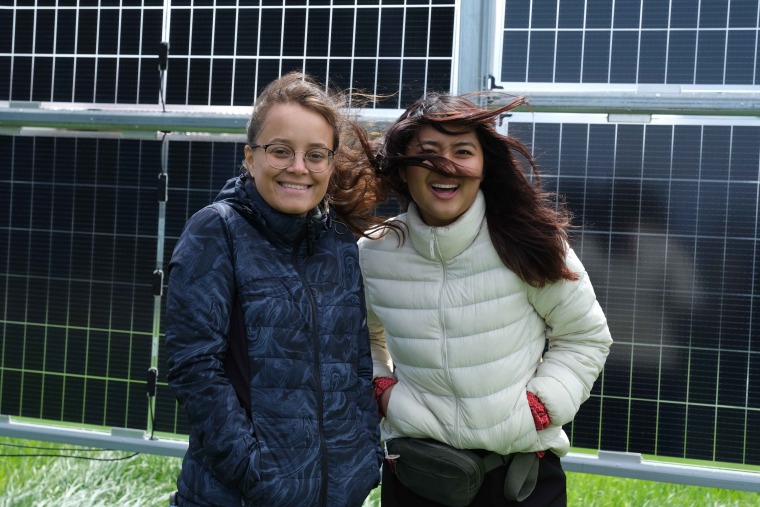 Nesrine Rouini in glasses and a blue jacket and Mira Kaibara smile in front of a solar panel installation during a field trip in South Korea.