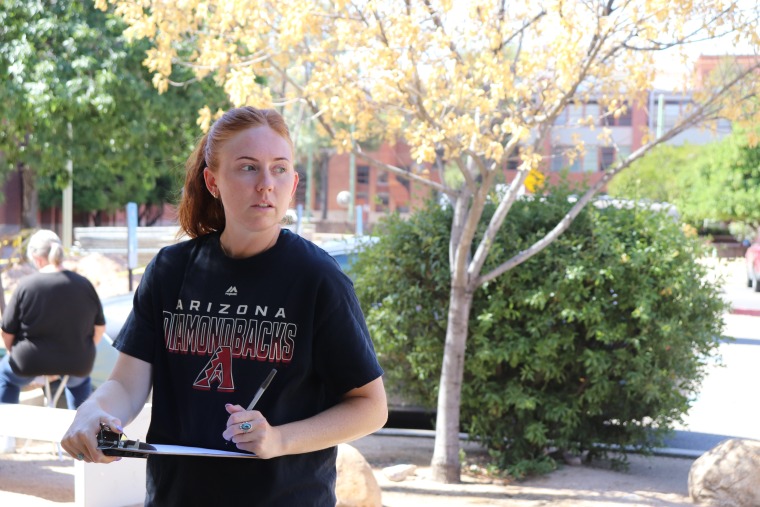 Emily Bartz wears a black t-shirt as she takes notes on a clipboard outdoors during the teacher workshop.