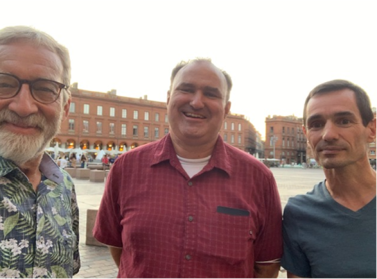 From left to right, Larry Fisher (floral shirt, black-rimmed glasses, goatee), Tom Meixner (red collared shirt), and CNRS lead François-Michel Le Tourneau pose in front of a water fountain and long red-brick building in Toulouse, France in September 2021.