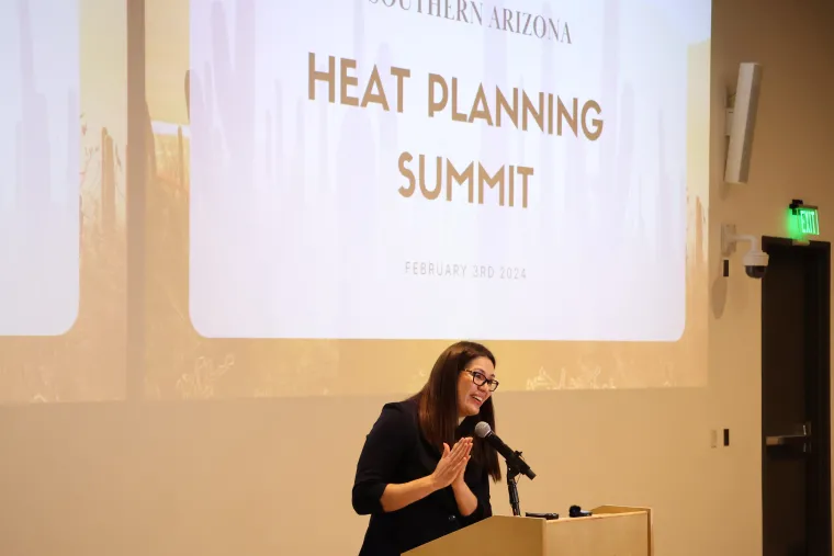 City of Tucson Chief Resilience Officer Fatima Luna claps and smiles while delivering opening remarks at the Summit. A slide projected on the wall behind her reads "Southern Arizona Heat Planning Summit" in black text.