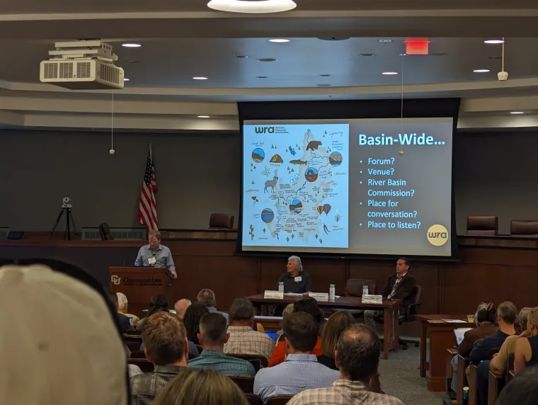 A projection screen shows a graphic depicting the many environmental stakeholders in the Colorado River Basin. Text on the right side of the image asks what types of basin-wide exchange need to happen.