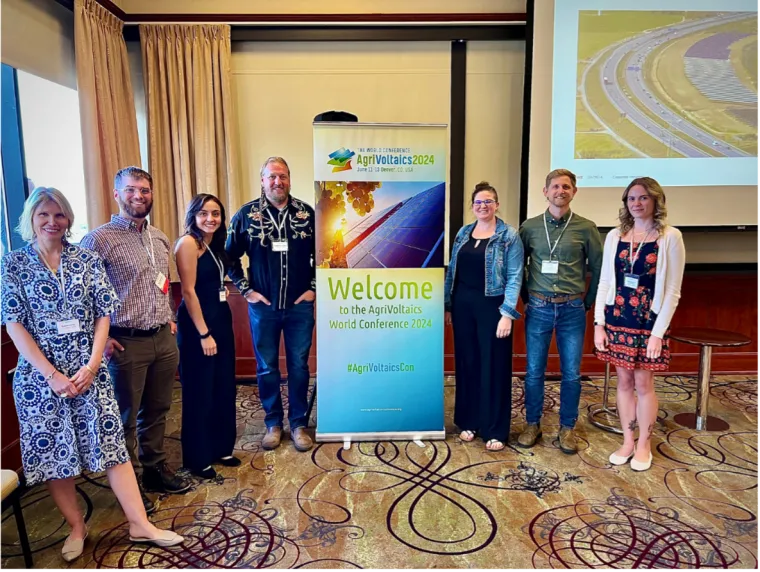 The UArizona research team poses with an AWC 2024 pop-up banner inside a conference room.