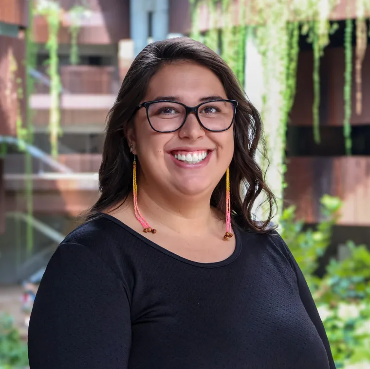 Carolina smiles in black framed glasses, a black shirt and beaded earrings at U of A's ENR2 building.