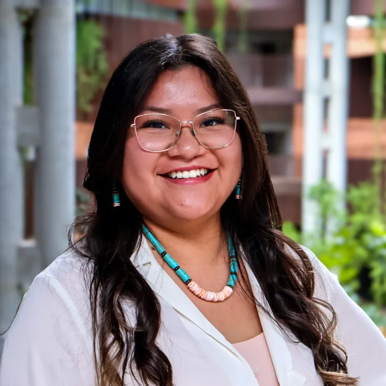 Kyra James smiles in a white blouse and turquoise bead necklace at U of A's ENR2 building.