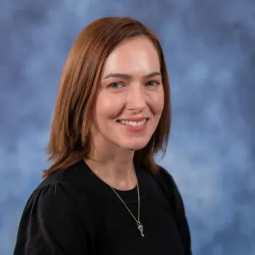 A portrait of Brewer-Osario in a black shirt against a blue backdrop.