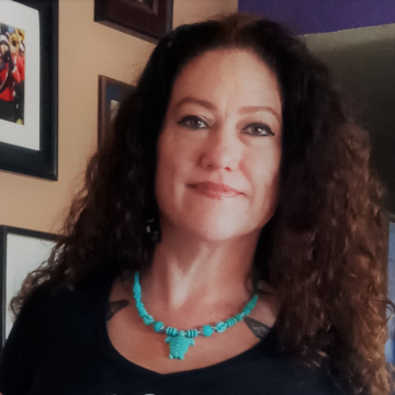 A portrait of Candi Inez-Cipactli Corral in a black top and turquoise neclack with a turtle pendant.