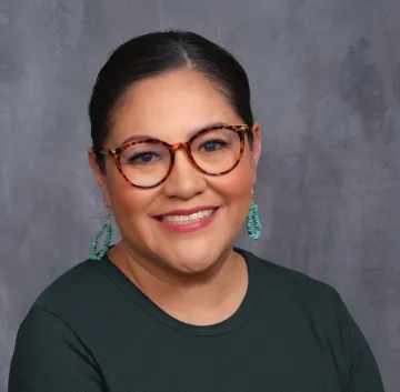 Crystal LoudHawk-Hedgepeth wear a dark green shirt, dangling turquoise earrings and red-rimmed glasses in this studio portrait.