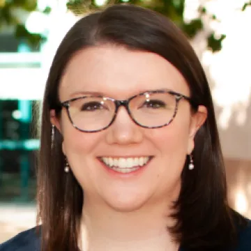 Portrait of Leslie Farland smiling in tortoise-shell glasses outdoors.