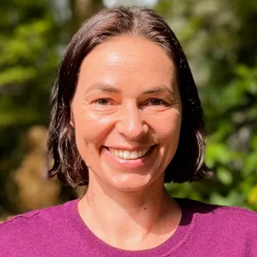 Headshot of Christine Van der Stege in a pink t-shirt outdoors in front of foliage.