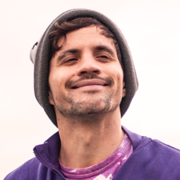 Portrait of Johnnie Sabin in a beanie and purple sweatshirt over a purple tie-dyed t-shirt against a white background.