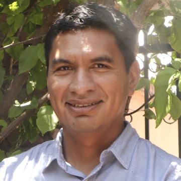 Headshot of Roberto Mendez-Arreola in front of an iron gate overgrown with foliage.