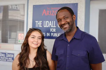 Ellie Claw and Ibrahim Garba pose for a photo by the blue Udall Center for Studies in Public Policy sign outside of the Center's main reception area.