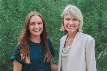 Ariada Woods and Andrea Gerlak pose outside of the Udall Center in front of a large, green shrub.