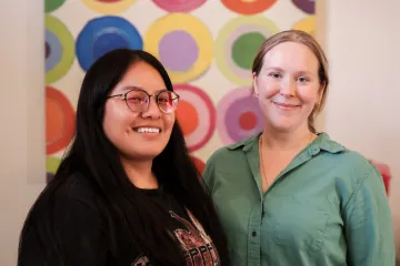 Trisha Jean Lane and Gemma Smith pose in front of an abstract painting of colorful circles arranged in a grid at the Udall Center.