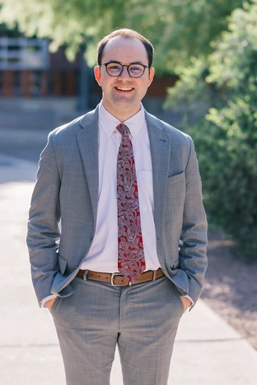 Abe Macy poses outdoors in a gray suit with his hands in his pockets