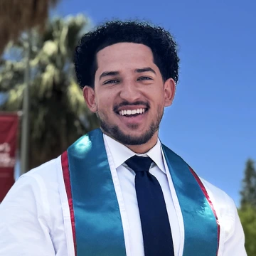 Levi Hood smiles on the U of A campus in a white shirt, black tie, and dark turquoise graduation stole