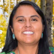 Portrait of Danya Carroll with turquoise earrings and trees in the background.