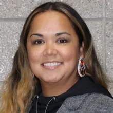 Portrait of Anna Ross in a black and gray hooded sweatshirt with concrete bricks in the background.