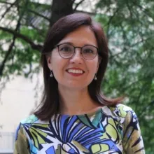 Adriana Zuniga-Teran poses outdoors in front of a tree in glasses and an abstract floral patterned blouse.