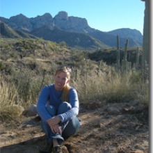 Arin Haverland rests on the ground in the Sonoran Desert with mountains in the background
