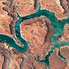 An aerial view of the Colorado River, a blue-green ribbon snakes through red canyons.
