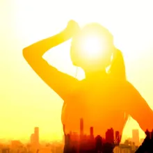 The semi-transparent silhouette of a young woman in front of a bright sun and city skyline.