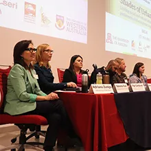 Adriana Zuniga-Teran, Natasha Pauli and others sit at a long table with a red curtain during a panel presentation.