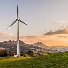 A modern windmill sits on a grassy hilltop near the coast at sunset.