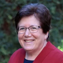 Sharon Megdal smiles in a red blazer outdoors in front of foliage.