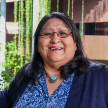 Joan Timeche smiles in a blue blouse, navy cardigan and turquoise necklace at U of A's ENR2 building.